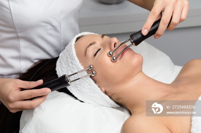 Beautiful woman receiving facial microcurrent treatment at spa salon. Beautician using electrical im