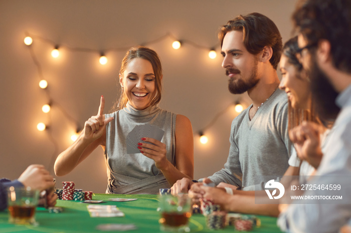 Happy young woman holds up finger as she has lucky hand in poker game with friends