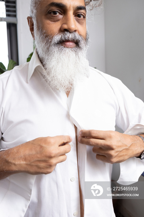 gray hair bearded man getting dressed in white shirt