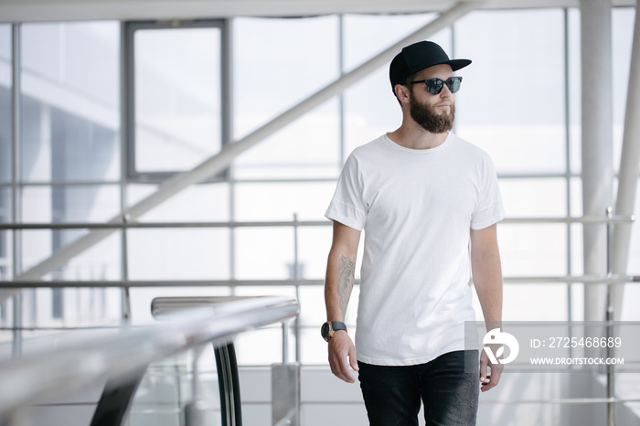 Hipster handsome male model with beard wearing white blank t-shirt and a baseball cap with space for