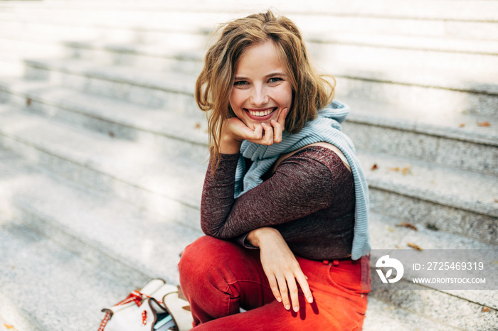 Cheerful student female smiling broadly, looking to the camera, sitting next to the college campus o