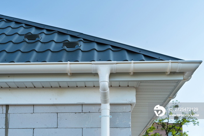 New metal tile roof with white rain gutter. SIP panel house construction. Unfinished building.