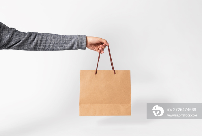 Hand holding blank brown paper bag for mockup template advertising and branding on gray background.