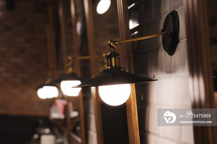 many copper lamp sconce hanging from white tile wall near big mirrors in beauty salon