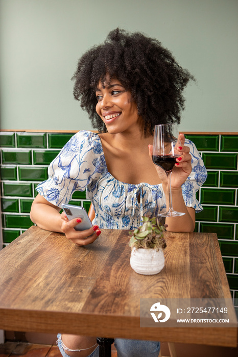 英国，伦敦，咖啡桌上拿着一杯红酒和智能手机的微笑女人
