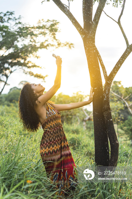 Imagen vertical de una mujer afroamericana de pie al lado de un árbol al aire libre realizando un ri