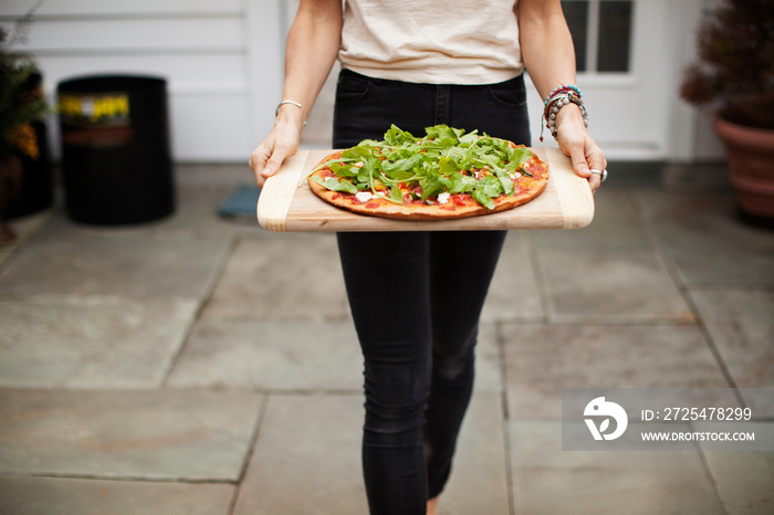 Mid section of woman carrying pizza on cutting board