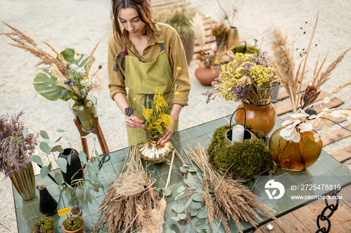 Young woman making compositions of dried and fresh flowers and herbs at the workshop outdoors. Flori