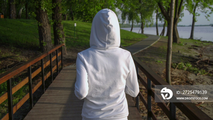 woman jogging along the forest lane. girl wears white hoodie.