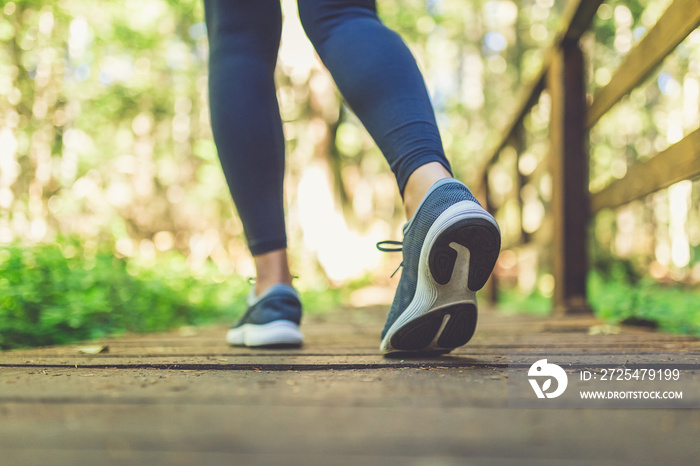 Close up of female legs with running shoes on wooden footpath in woods. Nature and sport healthy lif