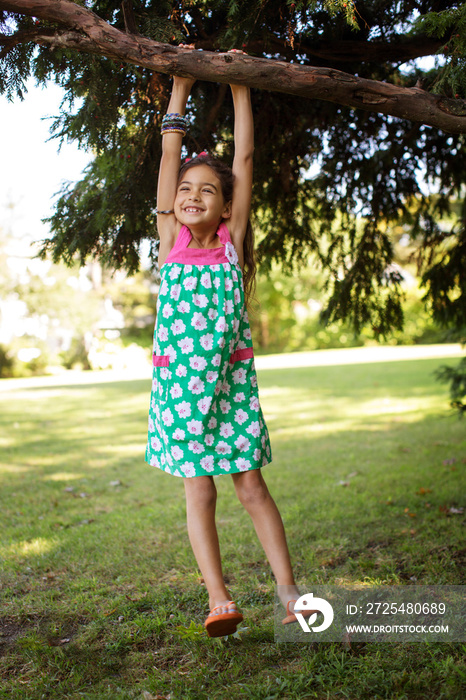 Girl (6-7) hanging on tree branch