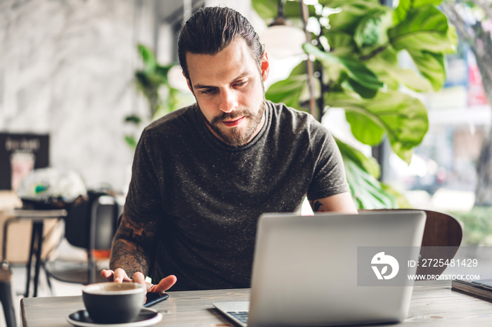 Handsome bearded hipster man use and looking at laptop computer with coffee at table in cafe.Communi