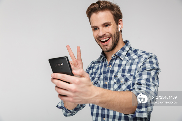 Portrait of happy young man gesturing peace sign while using cellphone
