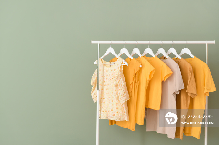 Rack with hanging clothes on color background