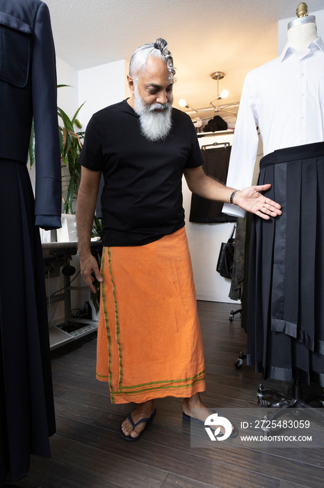 gray hair bearded man wearing skirt working in fashion design studio