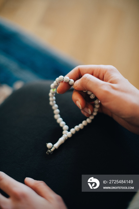 Cropped image of mature woman praying with rosary beads at home