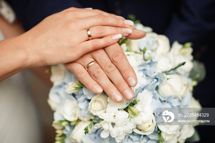 The bride and groom in wedding suits are holding together a wedding bouquet of white and lilac roses