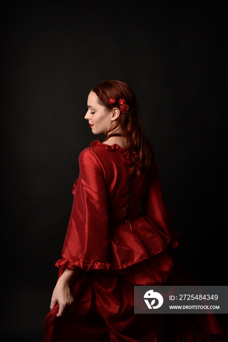 portrait of pretty female model with red hair wearing glamorous historical victorian red ballgown.  