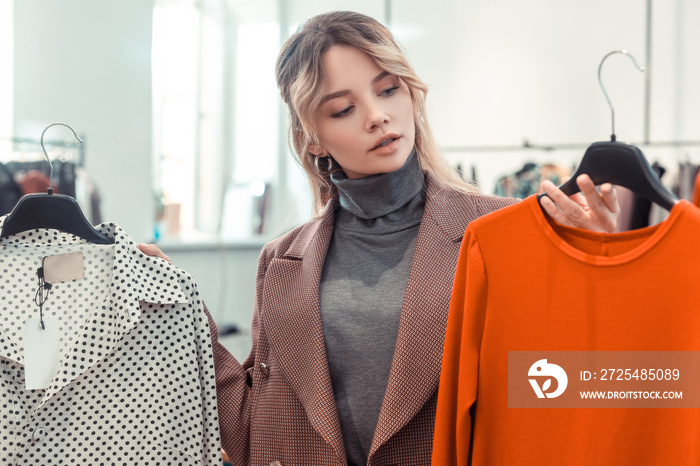 Blonde woman looking at bright orange dress while shopping