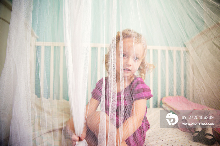 Small girl (2-3) sitting on bed behind canopy