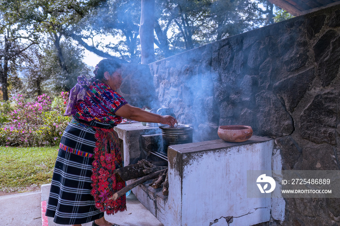 Mujer indigena con un vestido colorido, cocinando en  una estufa de leña.