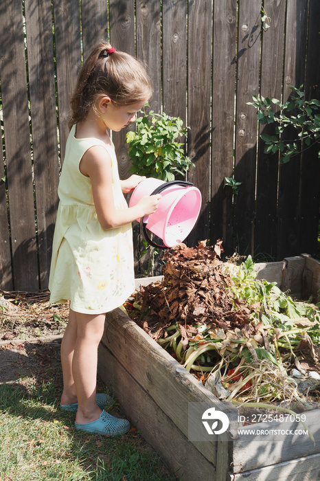 Little girl throws dry leaves in the compost bin. Separate sorting of garbage