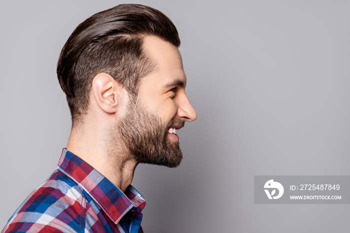 A side view portrait of young handsome smiling man with stylish haircut standing against gray backgr