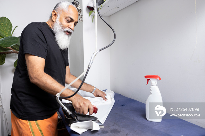 gray hair bearded man wearing skirt and ironing a white shirt