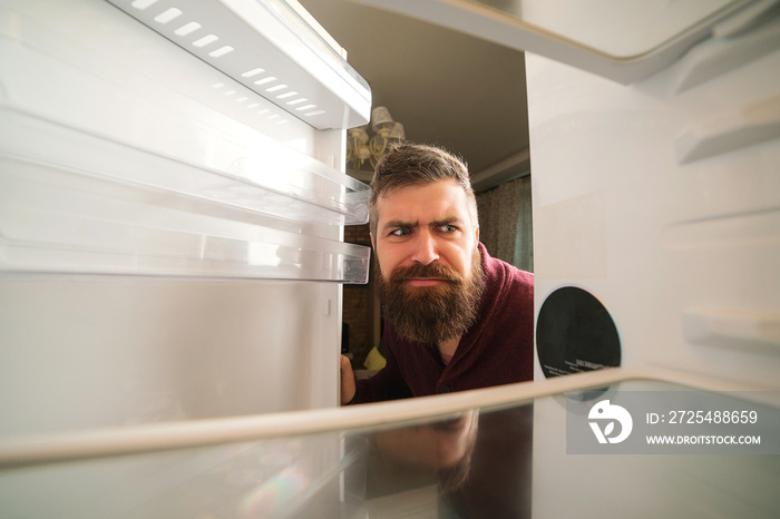 Hungry man looking for food in empty fridge. Man panics during coronavirus quarantine. Bearded man l