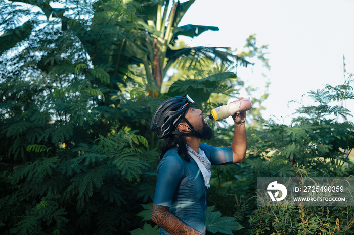 A young bearded cyclist drinking from a drinking bottle.