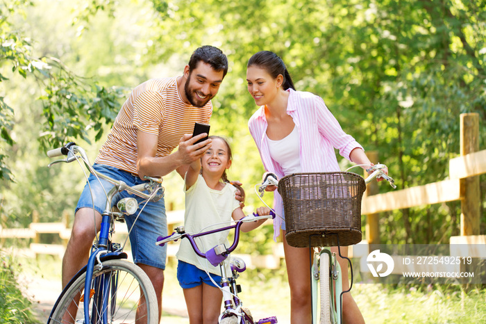 family, leisure and technology concept - happy mother, father and little daughter with smartphone an