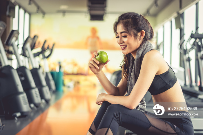 亚洲女性拿着绿苹果吃，背景是运动器材和跑步机