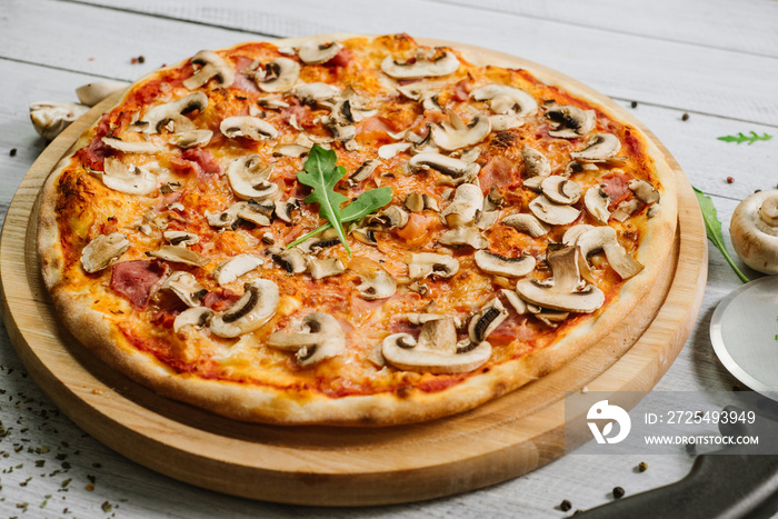 Tasty pizza Caprizzioza with tomato sauce, ham and champignons on the white wooden background