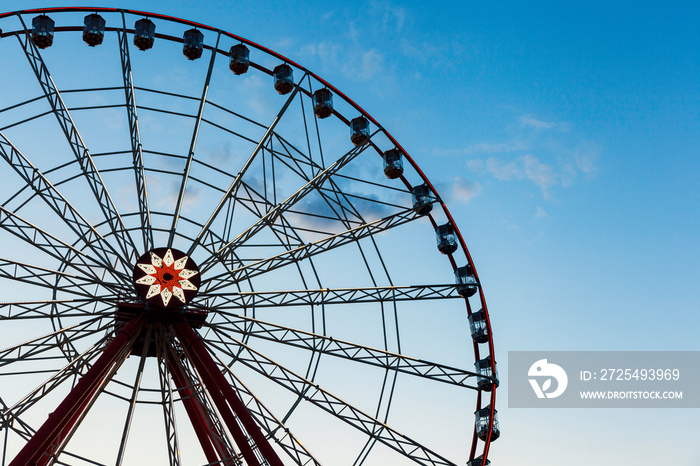 Huge ferris wheel and evening blue sky. Silhouette of a giant ferris wheel on the left.