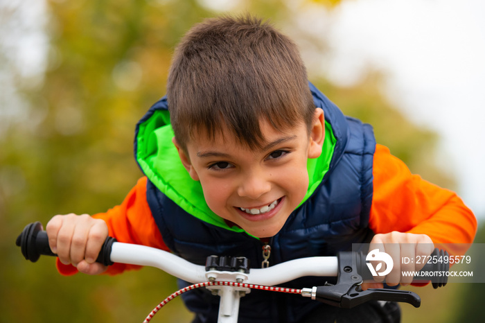 Portrait of a boy with a happy smile. Posing on a bicycle pedal in an autumn park. Active healthy ou