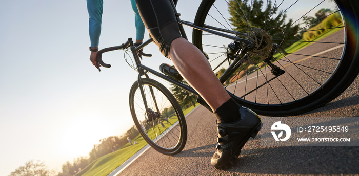 Close up of professional male cyclist in cycling shoes standing with his road bike on asphalt in par