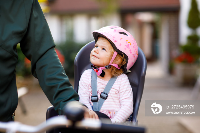 头戴安全帽的蹒跚学步的小女孩和她的父亲坐在自行车座椅上的肖像