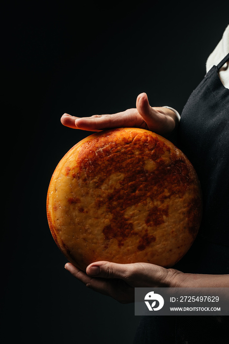 A head of hard cheese in mans cheesemaker hands. Different delicious dairy products