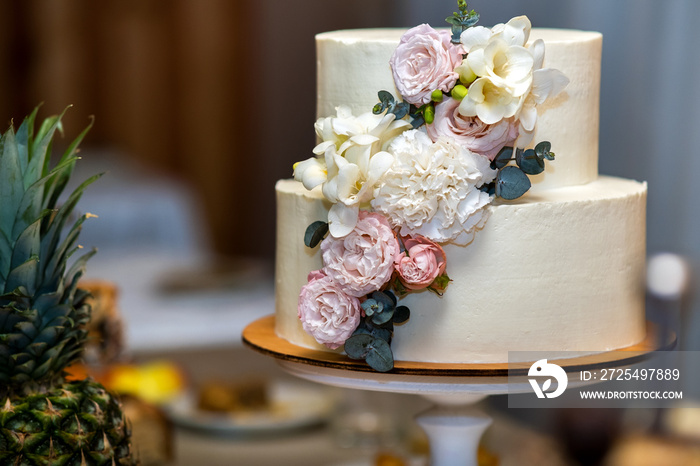 Tall sweet wedding cake decorated with live pink and white flowers on a table.