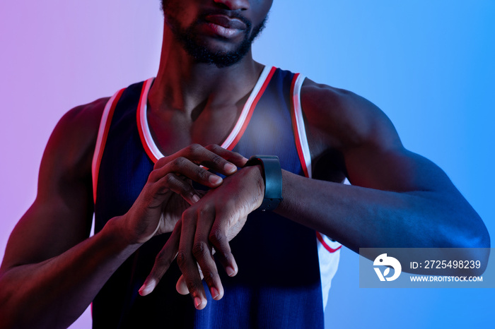 Cropped view of young black sportsman checking his smartwatch in neon light, closeup