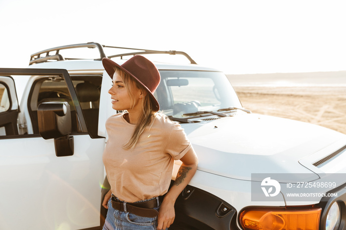 Beautiful young girl standing at the car at the sunny beach