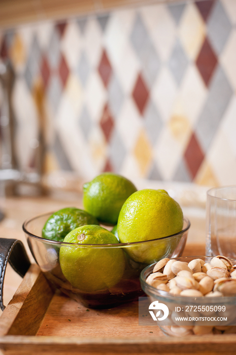 Close-up of oranges and pistachios in bowls against blurred backsplash on kitchen counter