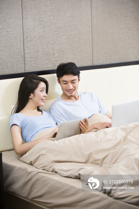 年轻夫妇在床上使用无线设备