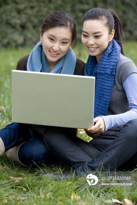 青年女子坐在草地上用电脑