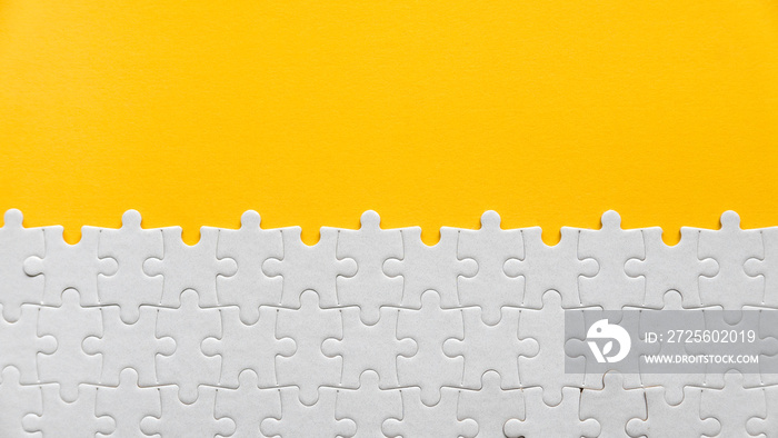 Top view of a white jigsaw puzzle on a yellow background with copy space.