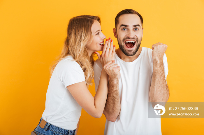 Image of amazed couple man and woman in basic t-shirts whispering secrets or gossips to each other