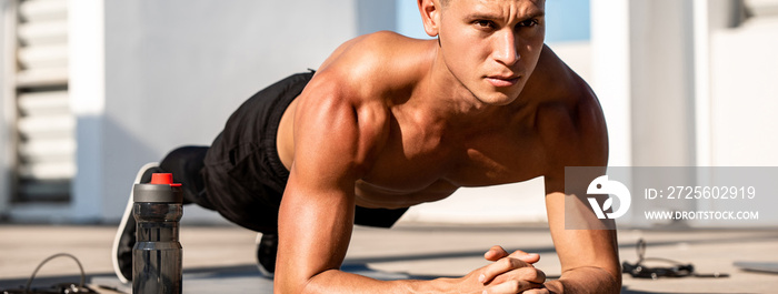 Banner image of handsome muscular sports man doing plank exercise outdoors on rooftop