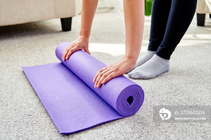 女性在运动练习、普拉提或工作后滚动紫色健身或瑜伽垫的特写图片
