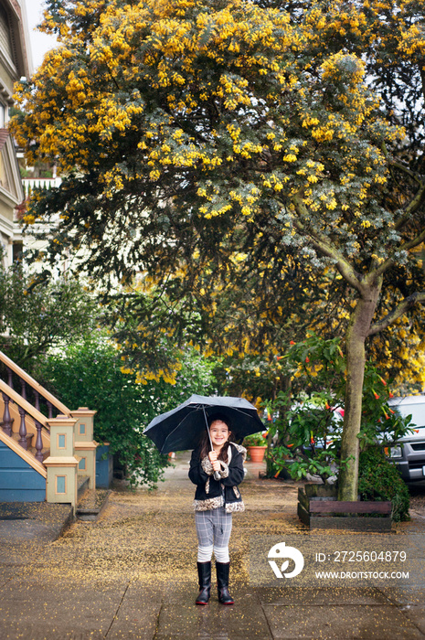 Girl (6-7) holding umbrella under flowering tree