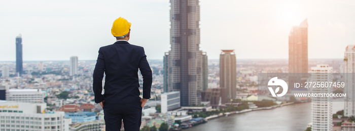 一名身穿黑色西装、头戴黄色头盔的建筑师站在建筑上寻找城市